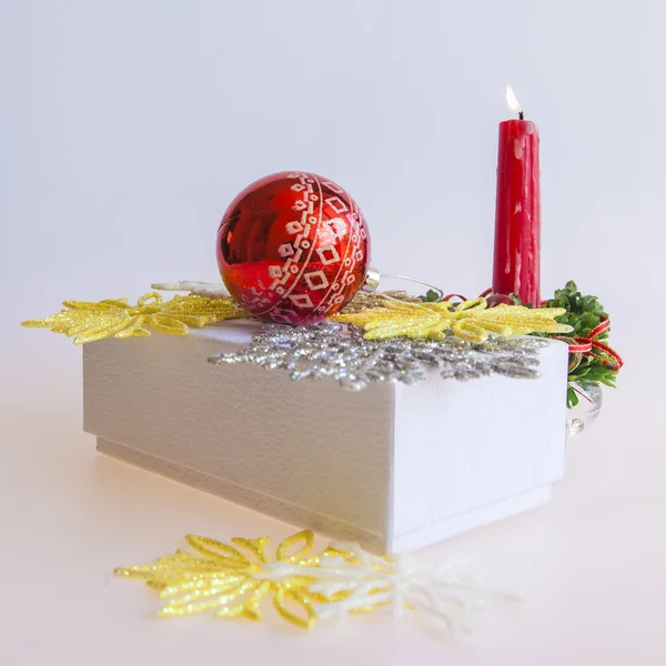 Neujahrsgeschenk in einem weißen Karton, Schmuck für einen Tannenbaum und eine brennende Kerze — Stockfoto