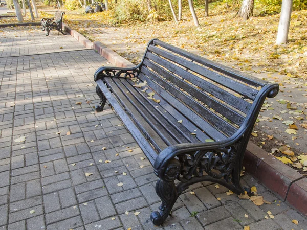 Скамейка с опавшими листьями в осеннем парке — стоковое фото