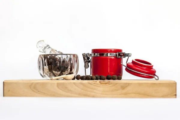 Black pepper in a transparent mortar with a pestle and the red container for spices — Stock Photo, Image