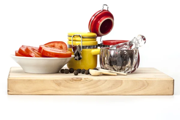 Pimenta preta em uma argamassa transparente com um pilão, fatias de tomate e recipientes multicoloridos para especiarias — Fotografia de Stock