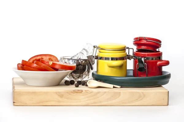 Svartpeppar i en transparent mortel med en mortelstöt, skivor tomat och flerfärgade behållare för kryddor — Stockfoto