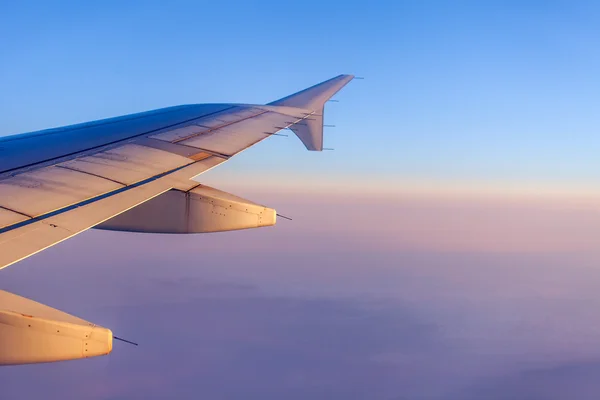 Flug bei Sonnenaufgang. Der Flügel des Flugzeugs und der Himmel leuchteten mit den Strahlen einer aufgehenden Sonne. Blick aus dem Fenster auf das Flugzeug — Stockfoto