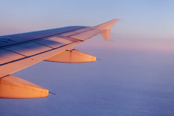 Gün doğumunda uçuş. Uçağın kanadı ve gökyüzü yükselen güneşin ışınlarıyla aydınlandı. Pencereden uçak görünümü — Stok fotoğraf
