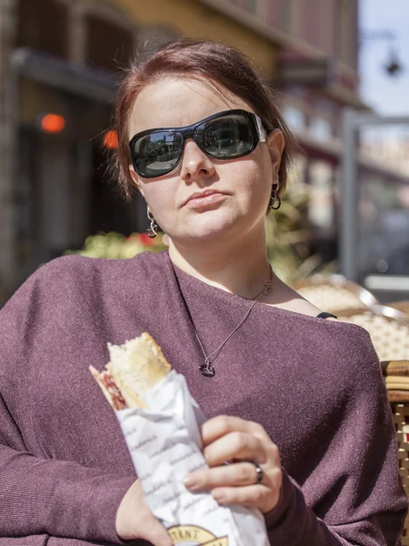 Piękna kobieta w ciemnych okularach w kawiarni ulicy zjada kanapkę — Zdjęcie stockowe