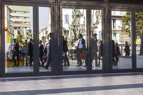 CANNES, FRANCE, on March 12, 2015. Типичный городской пейзаж. Улица и прохожие отражаются в стеклянной двери офисного центра — стоковое фото
