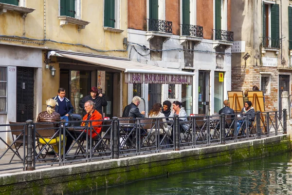 VENICE, ITALY - on MAY 1, 2015. Typical city landscape. People have a rest and eat in summer cafe on the bank of the channel — Stock Photo, Image