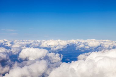 Bulutlar aşağıda ve parlak mavi gökyüzü uçan uçağın penceresinden görüntülemek