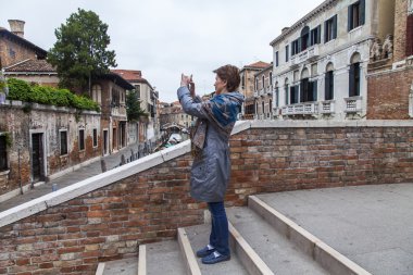 VENICE, ITALY on MAY 3, 2015. The bridge with steps via the channel. The tourist photographs sights