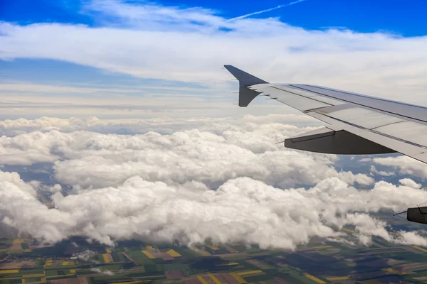 Blick aus dem Fenster des fliegenden Flugzeugs auf Wolken und eine Erdoberfläche darunter — Stockfoto