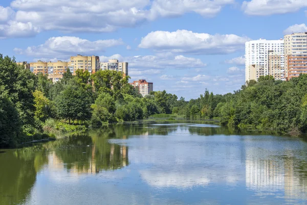 PUSHKINO, RÚSSIA, em 11 de agosto de 2015. Paisagem da cidade na tarde de verão. Casas de vários andares são refletidas no rio Serebryank — Fotografia de Stock