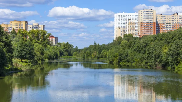 PUSHKINO, RUSSIA, on Aug 11, 2015. Городской пейзаж в летний полдень. Многоэтажные дома отражены в реке Серебрянк — стоковое фото