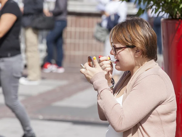 The young woman sits on the street on a bench and corrects a make-up