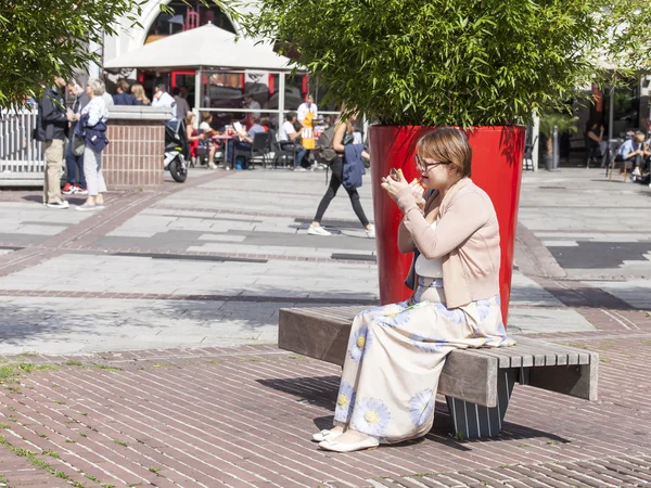 A jovem mulher senta-se na rua em um banco e corrige uma maquilagem — Fotografia de Stock