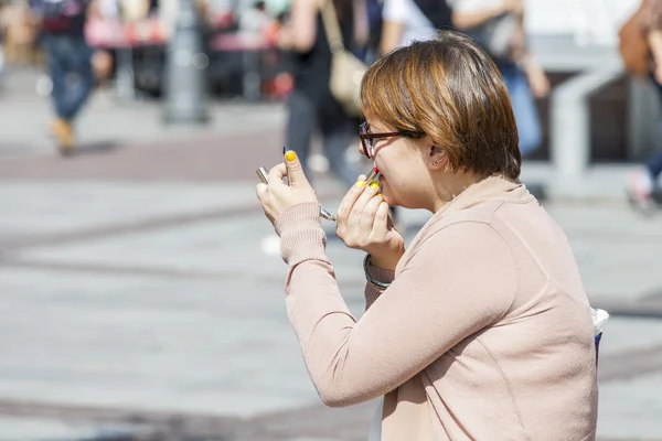 The young woman sits on the street on a bench and corrects a make-up