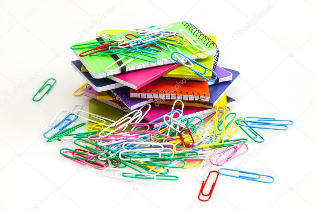 Rough pile of notebooks in covers of various colors and multi-colored paper clips