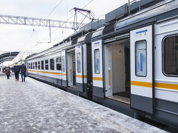 PUSHKINO, RUSSIA, on DECEMBER 17, 2015. Winter day. The suburban electric train stopped at a platform of the railway station. Passengers go on a platform — Stock Photo, Image