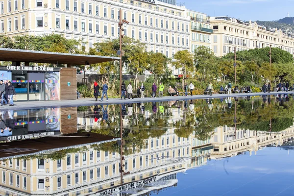 NICE, FRANCE, on JANUARY 7, 2016. The flat fountain in Promenade du Paillon park. An architectural complex of buildings in the boulevard and its reflection in water. People walk on a promenade