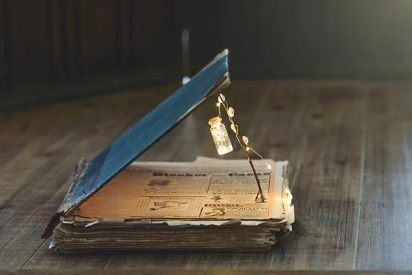 Open book with a miniature flashlight lies on a wooden table.