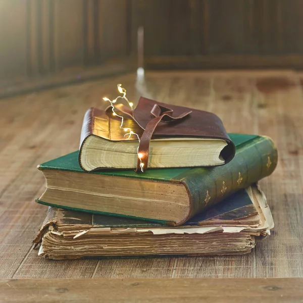 Books stack with a miniature flashlight lies on a wooden table.