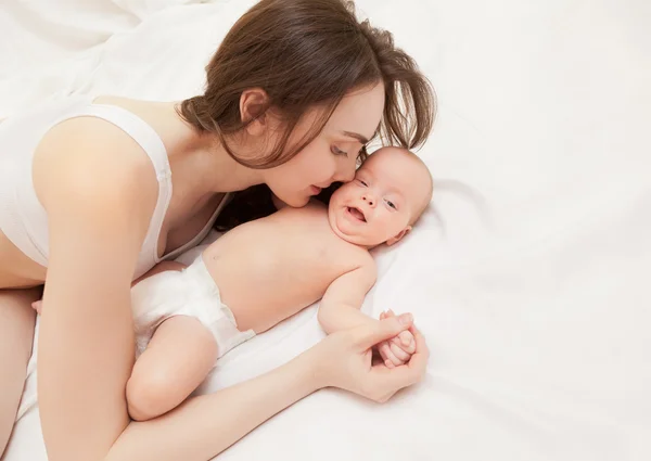 Foto de madre feliz besando a su bebé acostado en la cama — Foto de Stock