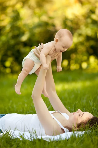 Happy woman holding in arm baby lying on grass — Stock Photo, Image