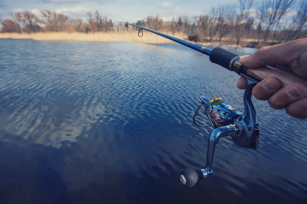 Hand with spinning and reel on the evening summer lake — Stock Photo, Image