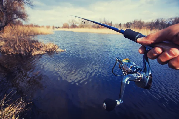 Hand with spinning and reel on the evening summer lake — Stock Photo, Image