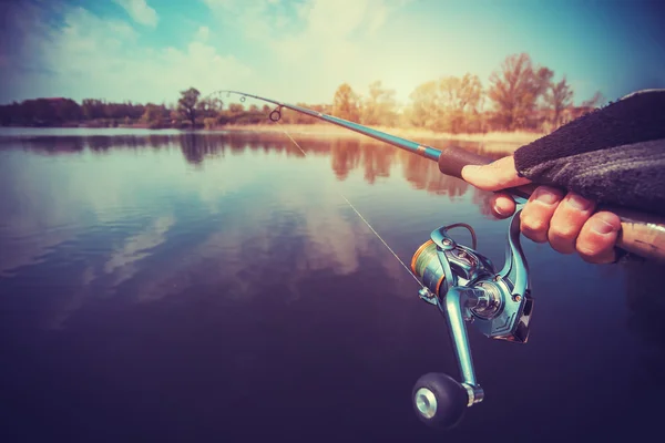 Hand with spinning and reel on the evening summer lake — Stock Photo, Image