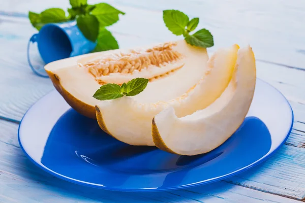 Melon doux frais dans une assiette bleue sur la table en bois blanc — Photo