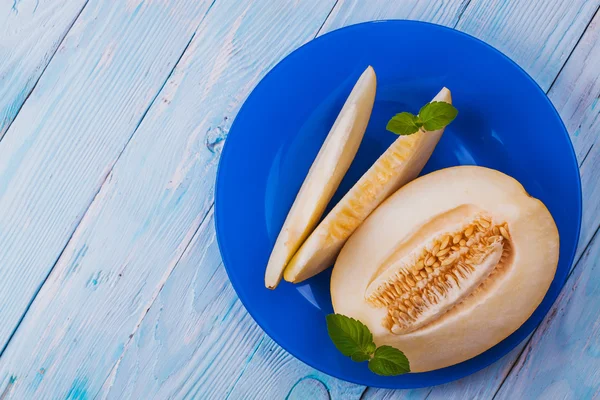 Melon doux frais dans une assiette bleue sur la table en bois blanc — Photo