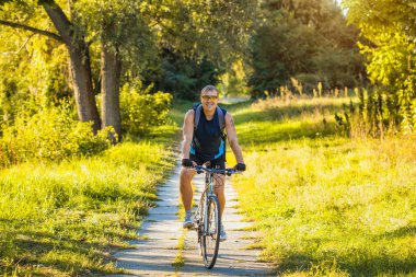 Bisikletli adam orman yolunda gidiyor.