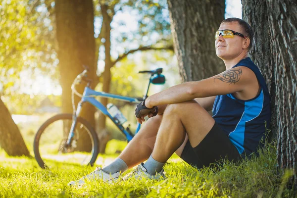 Ciclista descansando debaixo de uma árvore — Fotografia de Stock