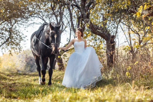 Mulher de vestido de noiva branco andando com um cavalo no parque de outono — Fotografia de Stock