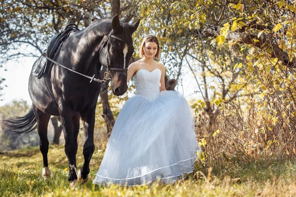 Mulher de vestido de noiva branco andando com um cavalo no parque de outono — Fotografia de Stock