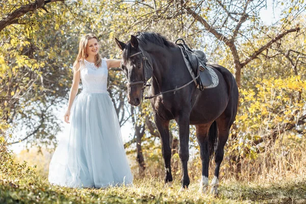 Kobieta w białej sukni ślubnej spaceruje z koniem w jesiennym parku — Zdjęcie stockowe