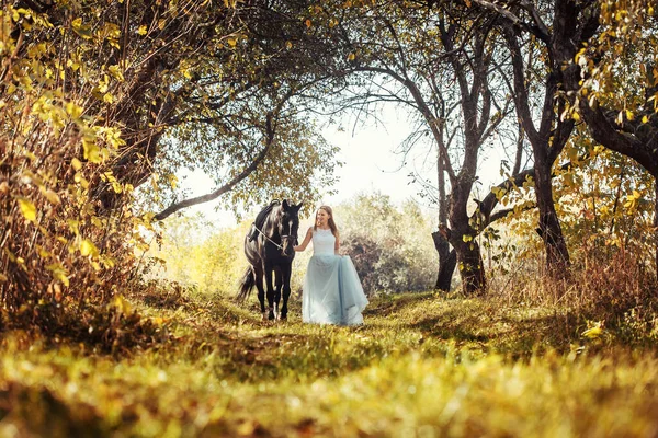 Žena v bílých svatebních šatech chůze s koněm v podzimním parku — Stock fotografie