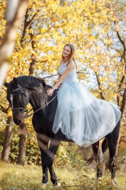 Beyaz gelinlikli bir kadın sonbahar parkında bir atla yürüyor.