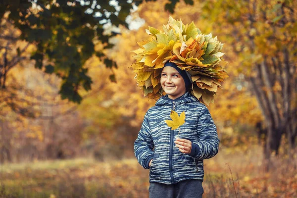 Gelukkig kind in de herfst bos het dragen van een krans van gele bladeren — Stockfoto