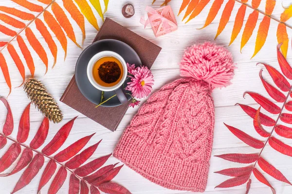 Livre, une tasse de thé chaud et un chapeau tricoté chaud, sur une table blanche en bois d'automne — Photo