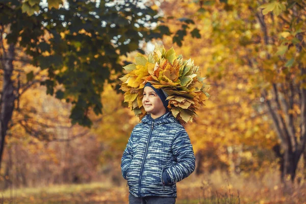 Gelukkig kind in de herfst bos het dragen van een krans van gele bladeren — Stockfoto