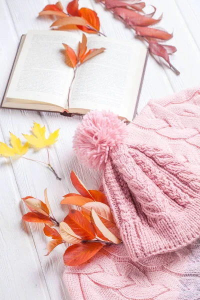 Książka i ciepły dzianina kapelusz i sweter, na jesienny drewniany biały stół — Zdjęcie stockowe