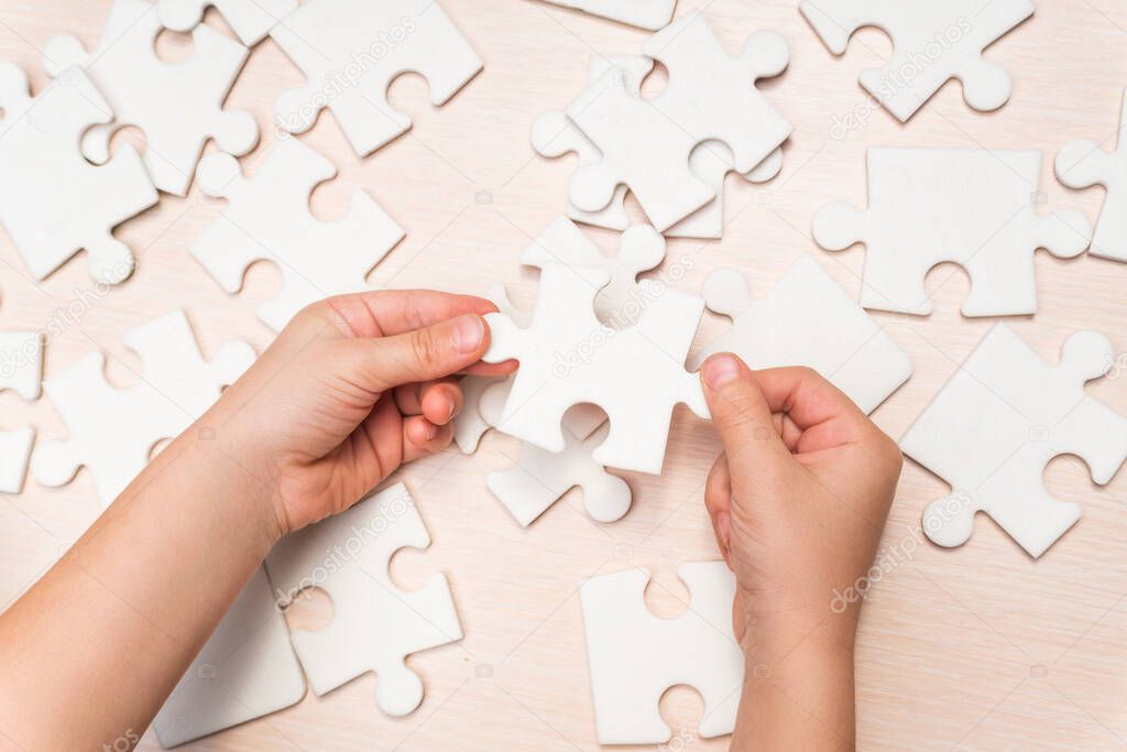 a child's hand makes the last missing piece of the puzzle on the table. strategy business concept