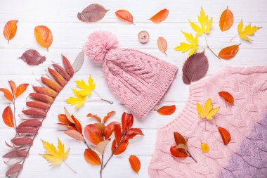 Kitap ve kalın bir örgü şapka ve süveter, sonbahar ahşap bir masa üzerinde. Sarı yapraklı sonbahar arkaplanı