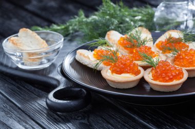 Tereyağlı tartlar, kırmızı havyar ve siyah tabakta dereotu.