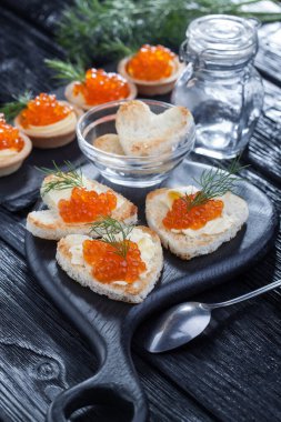 Yağ ve kırmızı havyarla servis edilen kalp şeklinde aperatifler siyah ahşap bir masada.