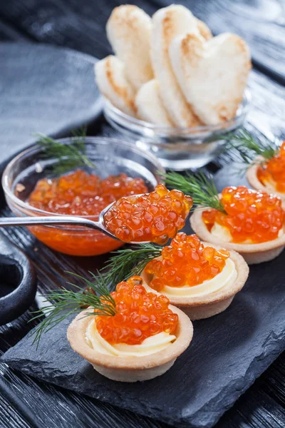 Tereyağlı tartlar, kırmızı havyar ve siyah ahşap bir masada dereotlar..
