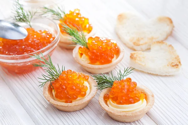 Tereyağlı tartlar ve kırmızı havyar ve beyaz ahşap masayı dereotla kaplayın..