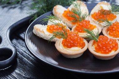 Tereyağlı tartlar, kırmızı havyar ve siyah tabakta dereotu.