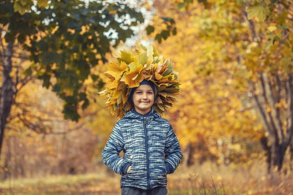 Niño feliz en el bosque de otoño con una corona de hojas amarillas — Foto de Stock