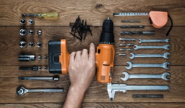 Kablosuz tornavida ve alet çantasını eski ahşap bir masada tutarken.